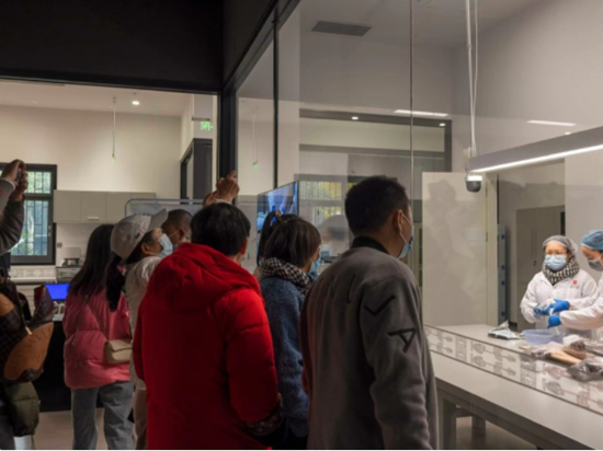 11月26日，象牙修復室內，兩名身穿白大褂的文物修復師正在進行象牙的修復工作。游客站在透明的玻璃墻外，可以看到修復的全過程