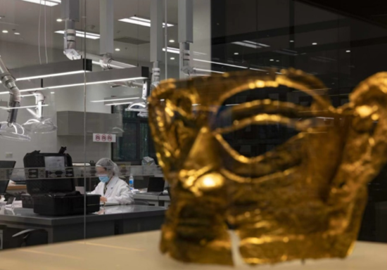 11月26日，今年三星堆遺址3號坑出土的金面具在文物修復館里與修復師隔空相望。
